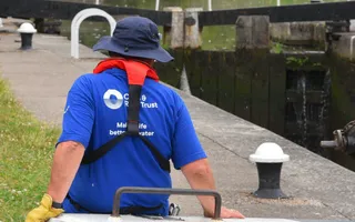 Man wearing blue shirt and hat with a lifejacket using a lock gate