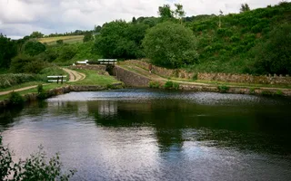 A vast expanse of water dominates the front of the shot, whilst a bridge leading up to a lock gate is in the distance surrounded by rolling green hills.