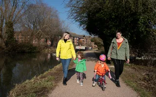 Two women wearing winter coats walking along the towpath with two children and a bike