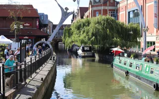 River running through town with boats on the right and people on a path on the left.