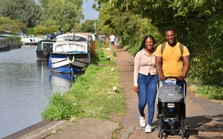 Two people smile as they push a pushchair along the towpath.