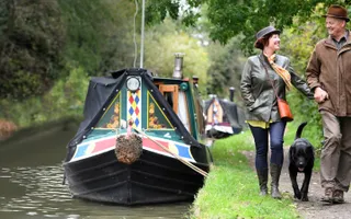 Two adults walk their dog on the canal towpath