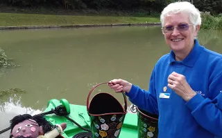 A Canal & River Trust volunteer on a narrowboat picks up a bucket painted with traditional canal roses
