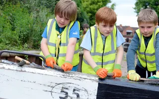 Three boys in Scout uniform and high vis brush down a lock gate