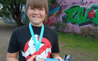 Young child grins cheekily as he holds a blue fishing medal and holds a certificate.