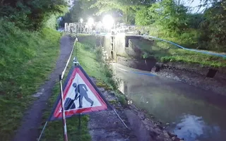 Warning sign showing digging on the towpath with a fenced off lock and floodlights showing repairs in progress