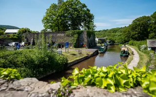 Sun shines on narrowboats moored on the towpath opposite a carpark
