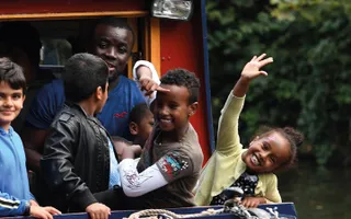 Children lean over the side of a narrowboat and raise their arms