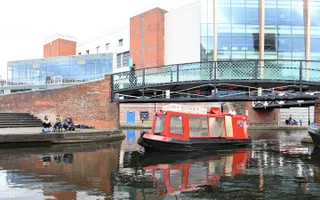 A small red boat with large windows moves through the Birmingham canals.