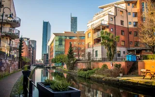 Urban canal winds between blocks of flats on a sunny day, with skyscrapers in the distance.