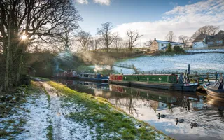 Wintery image of a canal with boats and patches of snow along the towpath