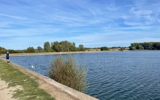 Wide shot of a reservoir on a sunny day with runner in the background