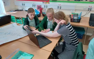 Two school children and teacher sitting around a laptop