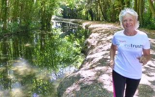 Woman running on the Grand Union Canal in dappled shade, surrounded by trees