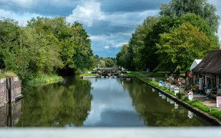 Looking over a bridge to a flight of locks with thick trees and a canalside cafe reflected in the canal.