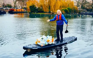 Comedian Bill Bailey stands on paddle board on the canal with a pile of plastic collected from the water