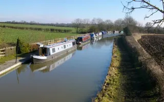 Boats moored along the towpath, surrounded by fields on a quiet stretch of the canal
