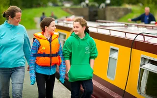 Three people walk along the towpath beside a hire boat