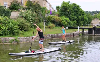 Two people standing on paddle boards outside a lock.