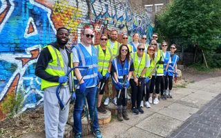 Line of volunteers wearing hi vis vests stand in front of a wall