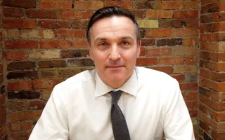 A man in a shirt and tie smiles at the camera.