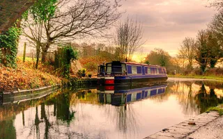 A narrow boat moors on the offside of the canal with the sunset reflecting on the water
