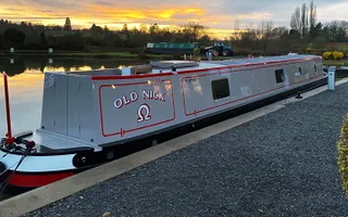 A brand new narrowboat, grey in colour with solar panels on top, on the canal at sunset