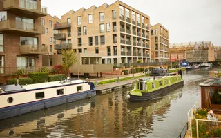 Narrowboat passes moored boats in a residential stretch of canal, surrounded by blocks of flats.