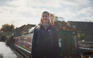 Portrait shot of a female ecologist standing in front of a moored narrowboat. She is smiling on a sunny winter's day