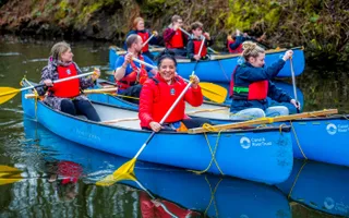 Group of people on bright blue canoes paddling on water.