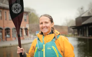 Woman posing for camera holding paddle and wearing yellow jacket