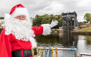 Person in Santa costume standing by water and boat lift with their arm extended outwards