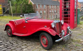 Old red vintage car on a cobbled street and red phone box behind