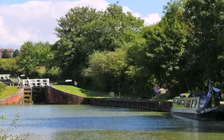 Narrowboat moors beneath trees at the bottom of a flight of locks.