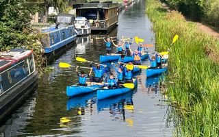 Group of young people paddling along the canal with paddles raised in the air