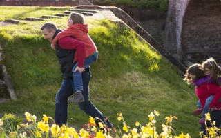 Two adults give piggy backs to children along the canal towpath
