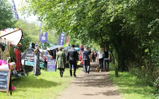 People walk along the towpath passed canal boats selling wares and decorated with signs.