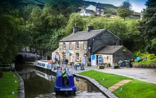 Wide shot of a canal with boats, old stone house and tunnel in the background