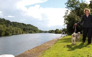 Lady walking dogs along grassy towpath next to canal