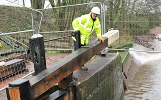 Colleague in high vis and a hard hat leans on a new lock beam next to a drained canal.