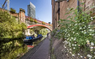 Wide shot of a towpath in an industrial area with flowers growing on the wall