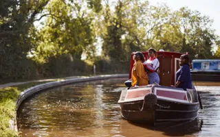 Three people sit in the front of a narrowboat on a sunny day.