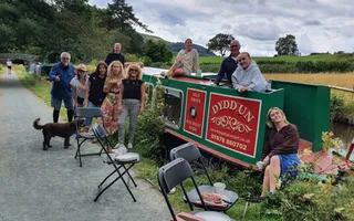 A group of people gather round a narrowboat smiling for the camera. A dog stands nearby