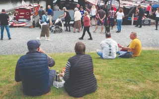 People sitting on grass beside a large crowd next to the canal on a sunny day