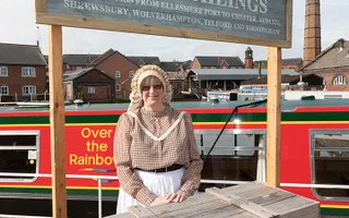 A museum volunteer in period costume stands at a kiosk at the National Waterways Museum