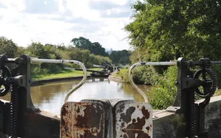 The picture is taken from behind a lock gate, directly ahead there are other lock gates with grass and hedgerows lining the canal.