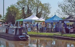 Group of people observing stalls along the towpath with boat driving past