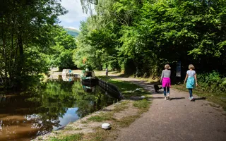Two people on a sunny day walking along the towpath next to a canal