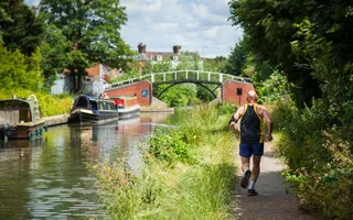 Sunny day, a man is running along the towpath by the canal. Boats and bridges in the distance
