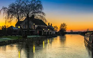 A canal scene with a moored narrowboat and house on the offside beneath a rich sunset